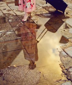 a woman with an umbrella is standing in the rain and reflecting on the wet ground