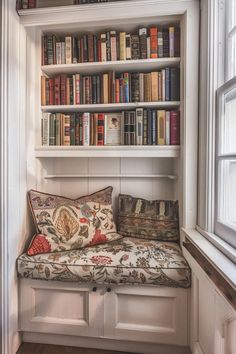 a window seat in front of a bookshelf filled with lots of books and pillows