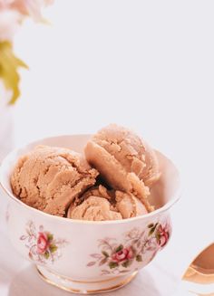 two scoops of ice cream sit in a bowl with flowers on the table next to it