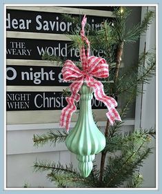 a green vase with a bow on it sitting next to a christmas tree in front of a sign