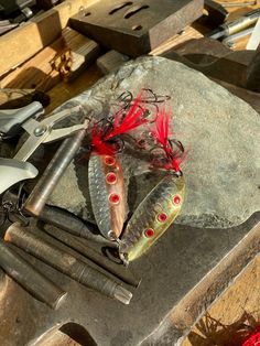 two fish with red eyes are sitting on a rock next to some knives and other tools