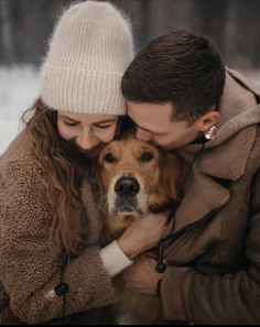 a couple cuddles with their dog in the snow while holding each other's head