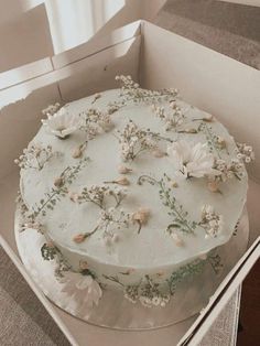 a cake in a box with white flowers on it and greenery around the edges