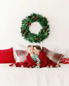 two children sitting on a bed under a christmas wreath