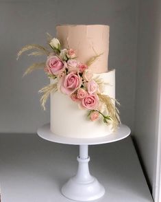 a three tiered cake with pink flowers on top is sitting on a white pedestal