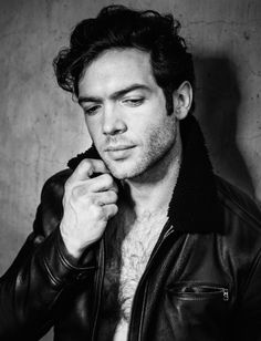 a black and white photo of a man in a leather jacket leaning against a wall