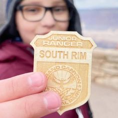 a person holding up a wooden badge with the words junior ranger south rim on it