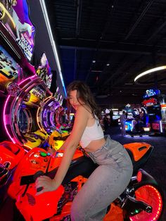 a woman sitting on top of a motorcycle in a pinball game room with neon lights