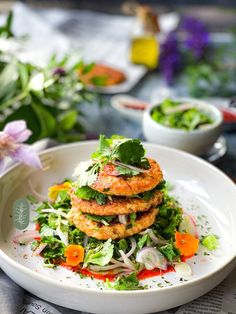 a white plate topped with crab cakes and veggies next to a bowl of salad