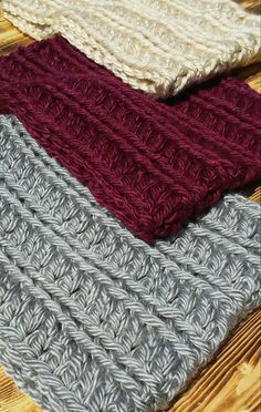 four knitted scarves sitting on top of a wooden table