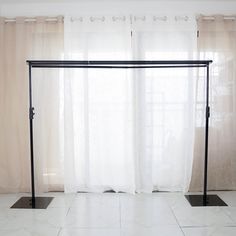 an empty room with white tile flooring and curtained window behind the bed frame