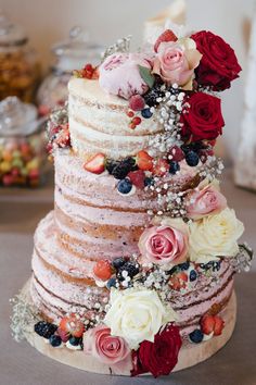 a multi layer cake with flowers and berries on it's top is sitting on a table