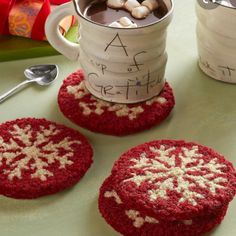 three crocheted coasters sitting on top of a table next to two mugs filled with hot chocolate