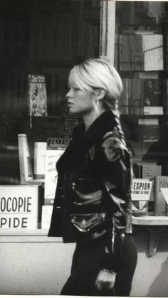 black and white photograph of a woman walking in front of a book store with bookshelves behind her