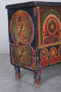 an artisticly painted wooden cabinet with decorative designs on the front and sides, sitting on a tile floor