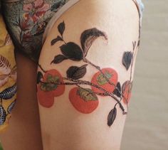 a woman's thigh with tattoos on her legs and an apple branch painted on it