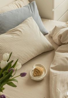 a bowl of croissants sits on a bed with pillows and plaid sheets