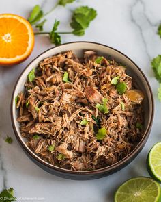 a bowl filled with shredded meat and garnished with cilantro next to sliced oranges