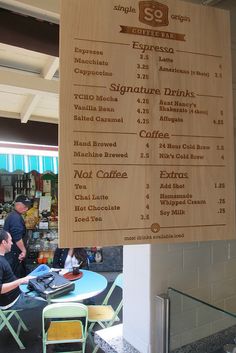 a menu hanging from the side of a wall in front of a table with people sitting at it