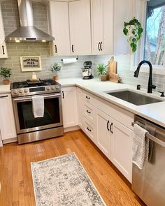 a clean kitchen with white cabinets and stainless steel stove top oven, dishwasher, sink, and rug