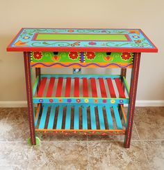 a brightly colored wooden table with flowers painted on the top and bottom shelf, in front of a beige wall