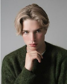 a woman with blonde hair wearing a green sweater and posing for a photo in front of a gray background