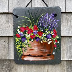 a painting of flowers in a pot hanging on a wooden wall next to a building