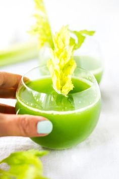 a woman's hand holding a green drink in a small glass with a leaf sticking out of it