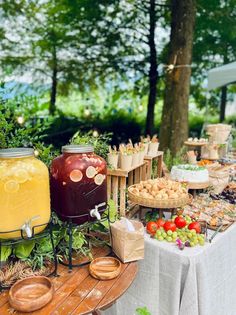 an outdoor picnic with food and drinks on the table in front of some trees,