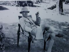 an old man sitting in a chair with his foot on the ground and holding something up