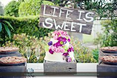 a wedding cake with flowers on top and cookies in the foreground at a garden party