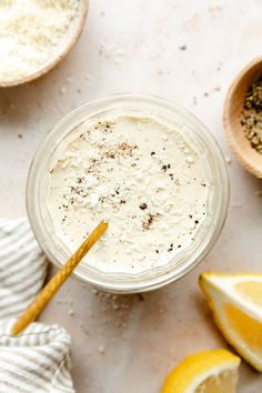 a glass jar filled with white liquid next to sliced lemons and spices on a table