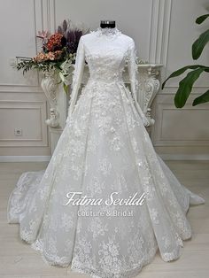 a white wedding gown with long sleeves and lace on the skirt is displayed in front of a