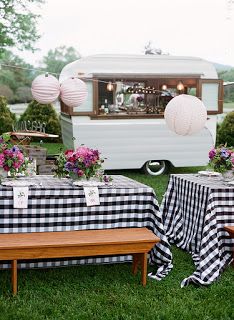 a picnic table with black and white checkered cloth on it, next to an old camper