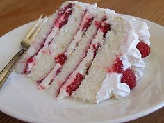 a white plate topped with a slice of cake covered in whipped cream and raspberries