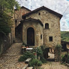 an old stone building sitting on the side of a cobblestone road next to trees