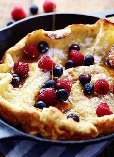 a pancake with berries and blueberries is being drizzled with syrup