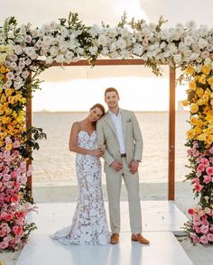 a man and woman standing in front of a floral arch