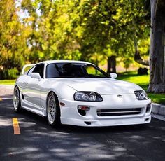 a white sports car is parked on the side of the road in front of some trees