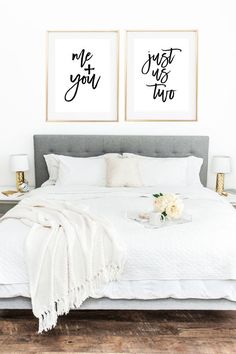 a white bed with two framed pictures above it and flowers on the end table next to it