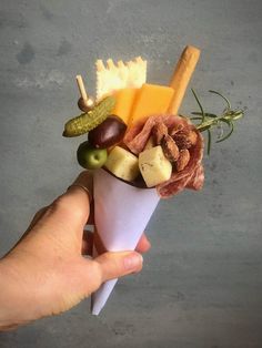 a hand holding an ice cream cone filled with different types of fruit and cheeses