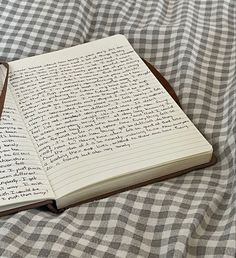 an open notebook sitting on top of a checkered tablecloth covered bed with writing