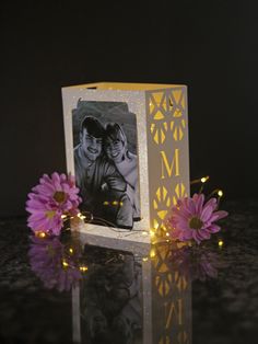 a small white box with a photo on it next to some pink flowers and lights