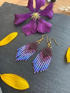 two pairs of purple and blue beaded earrings next to a flower on a slate slab