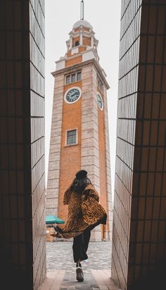 a woman is standing in front of a tall tower with a clock on it's side