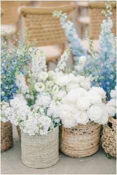 white and blue flowers are sitting in baskets on the ground next to wicker chairs