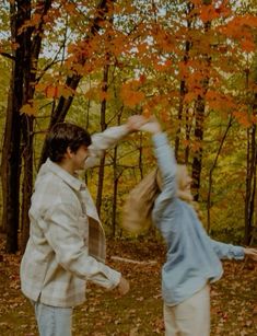 two people are dancing in the woods with leaves on the ground and trees behind them