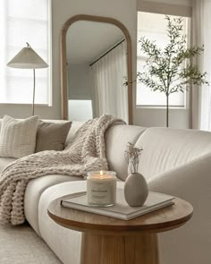 a white couch sitting next to a table with a candle on it in front of a mirror