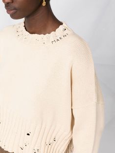 a woman in a white sweater and gold earrings is looking off to the side with her hand on her hip