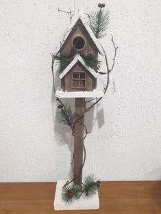 a birdhouse is decorated with pine branches and evergreens on a wooden table next to a white wall